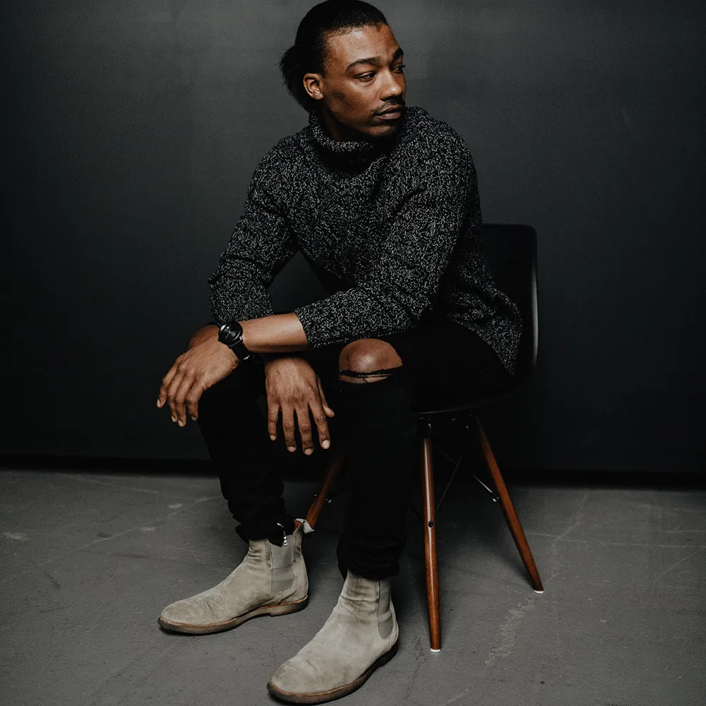 Sitting on a wooden chair in a dark marled knit, a black Aspect on black leather