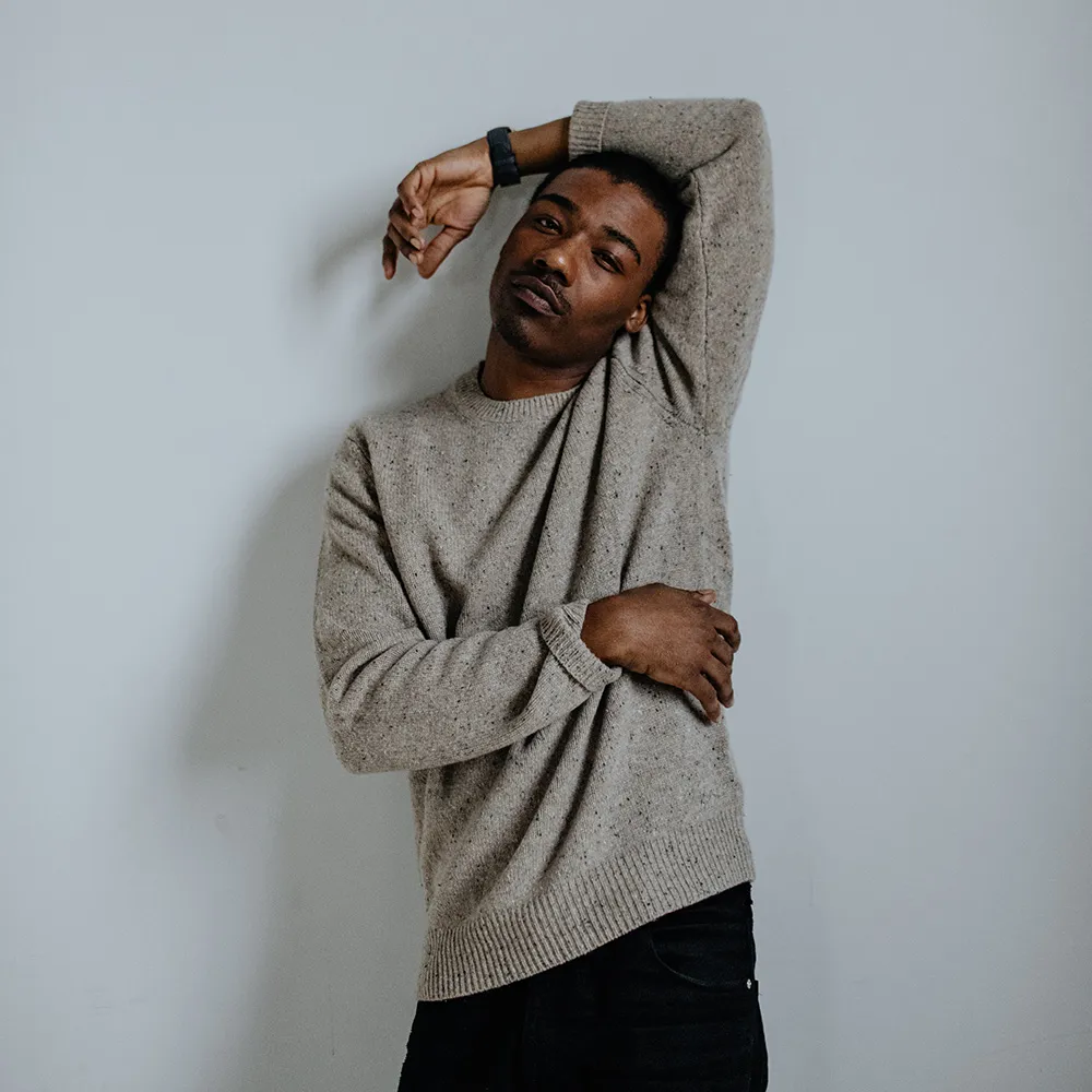 An arm raised overhead in an oatmeal sweater, a rose gold Aspect at the wrist