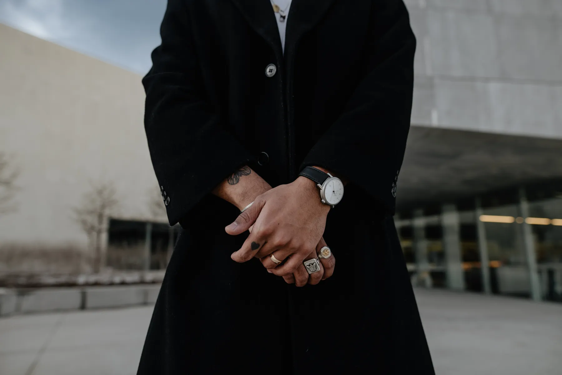 Hands folded over a long black coat, a silver Aspect on black leather