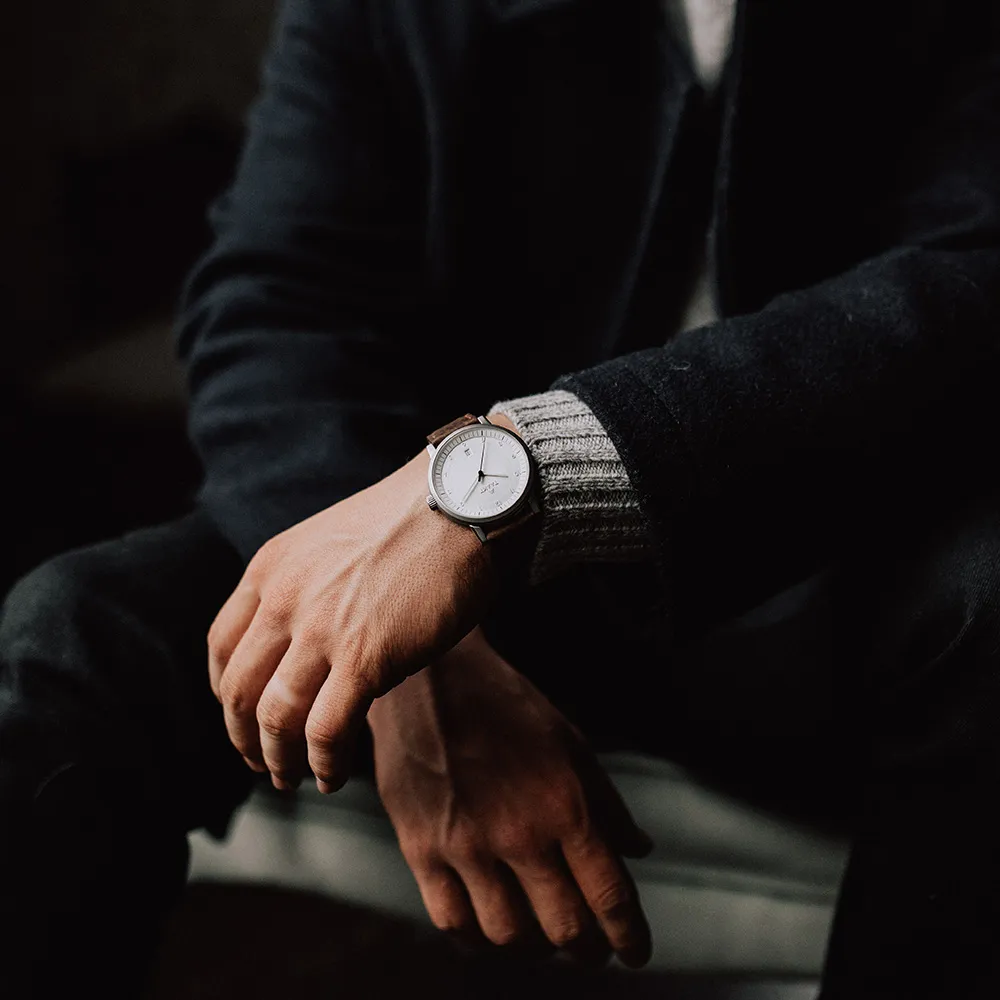 Seated in a dark jacket over a knit cuff, a silver Aspect on brown leather